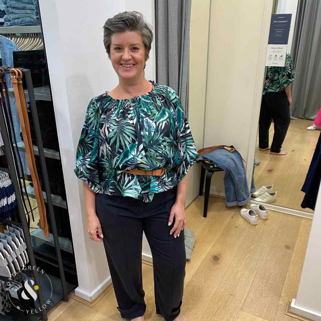 Women wearing top with green tropical print belted with a beige belt worn over blue pants