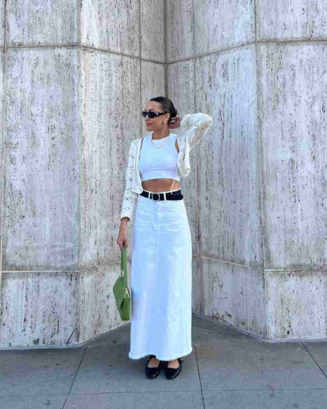 Women wearing a white maxi skirt; cropped whit t-shirt and cardigan; wide black belt, green handbag and black Mary Jane shoes