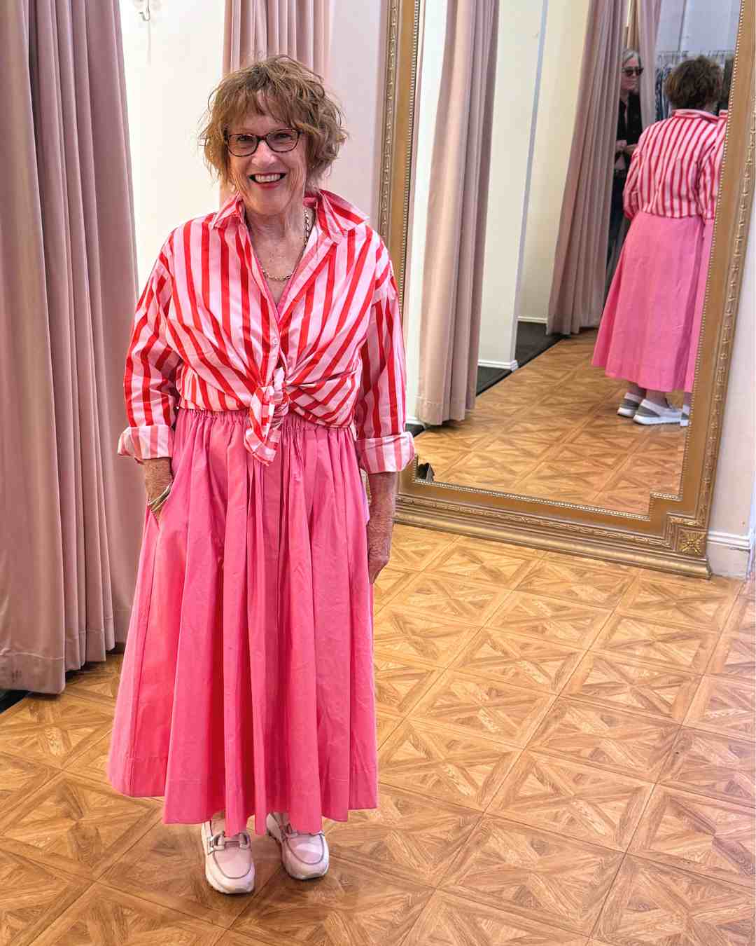 Women wearing a pink and red striped button down shirt tied at the waist over a pink maxi dress
